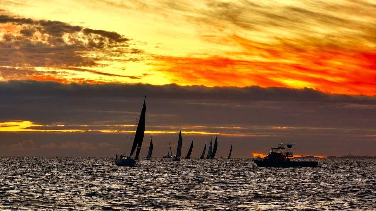 Fleet of sailing boats silhouetted against a fiery sunset sky