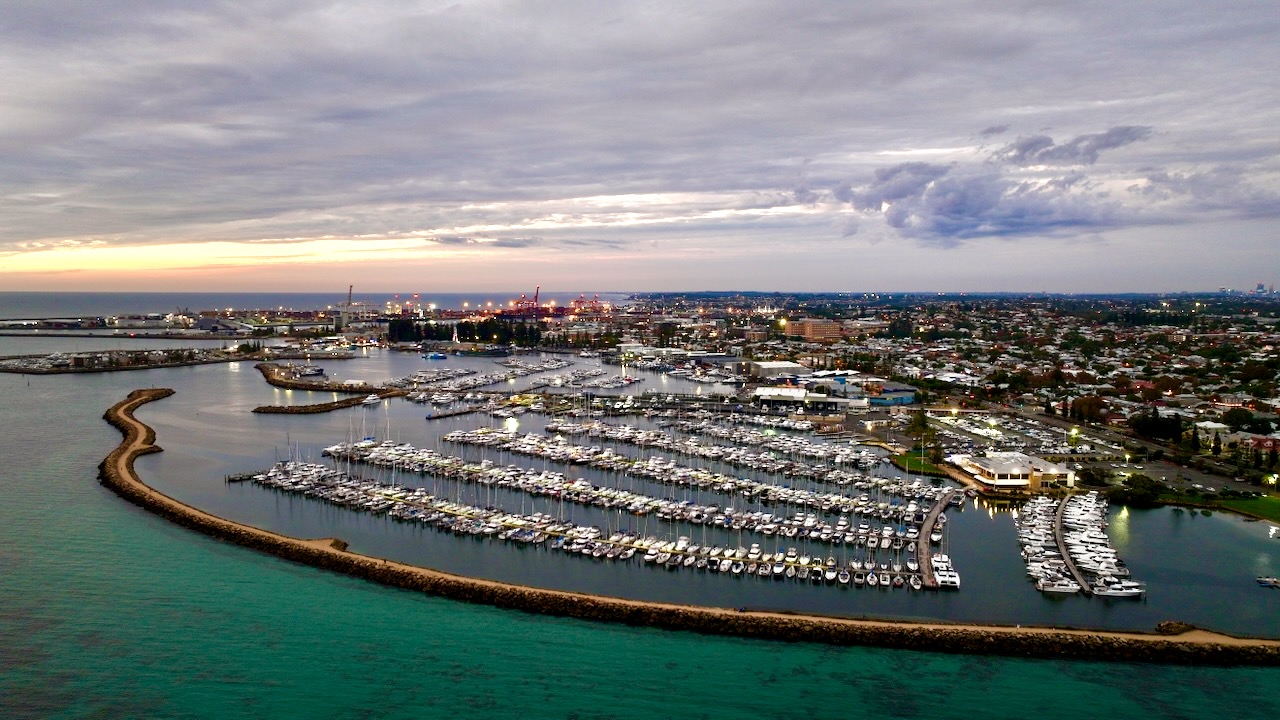 Aerial panorama of a marina at dusk with the port lit in the distance